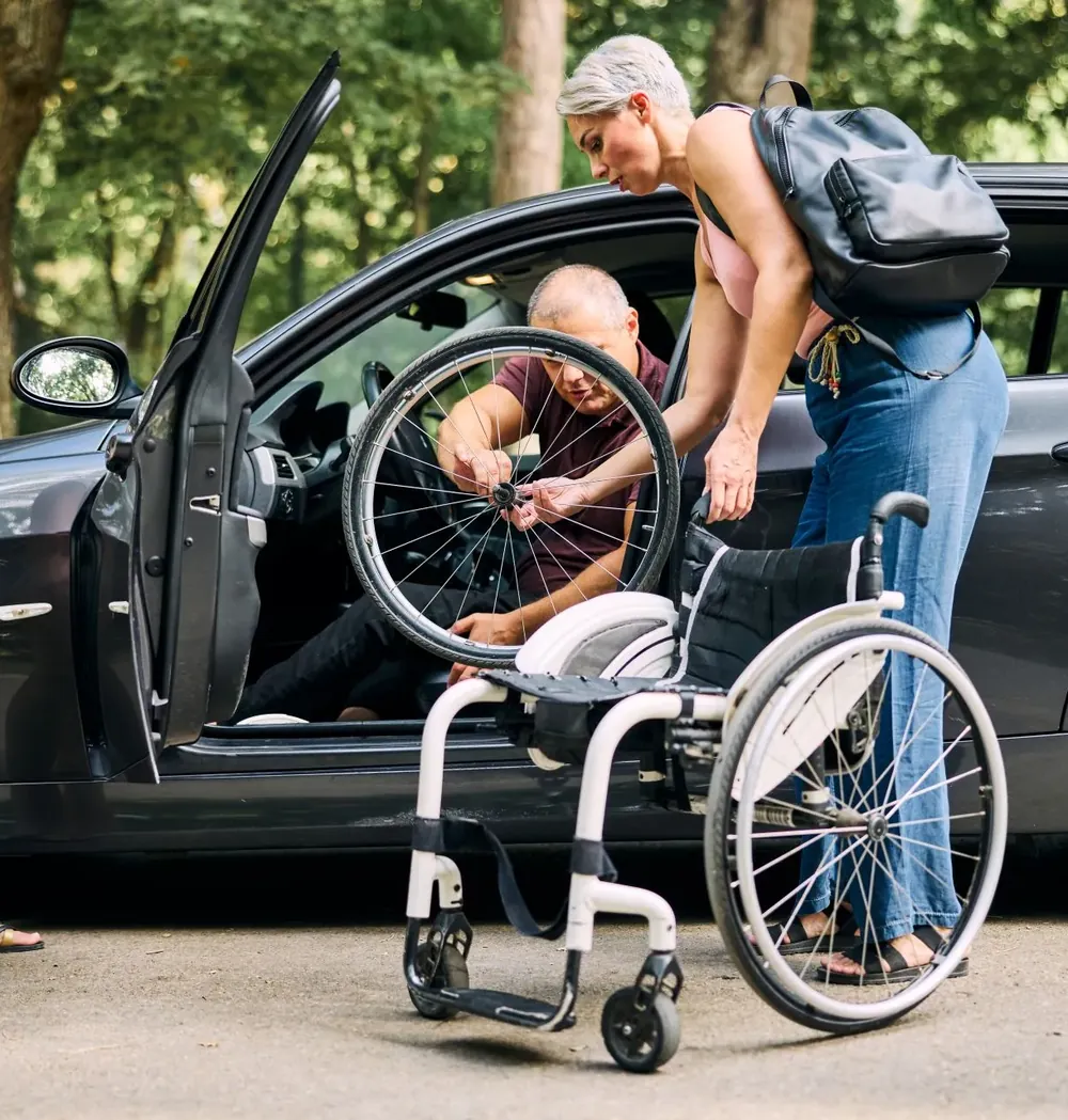A woman helping a man assemble his wheelchair beside his car